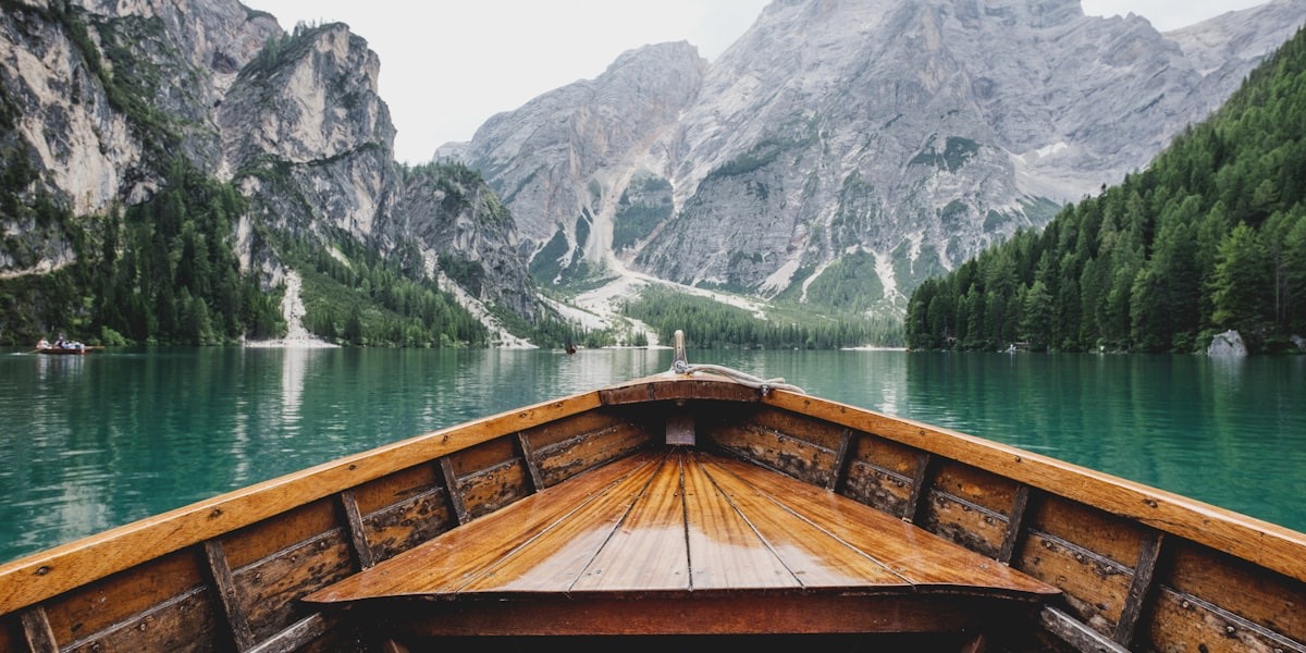Proue d'une barque en bois fendant l'eau turquoise d'un lac de montagne entouré de sommets