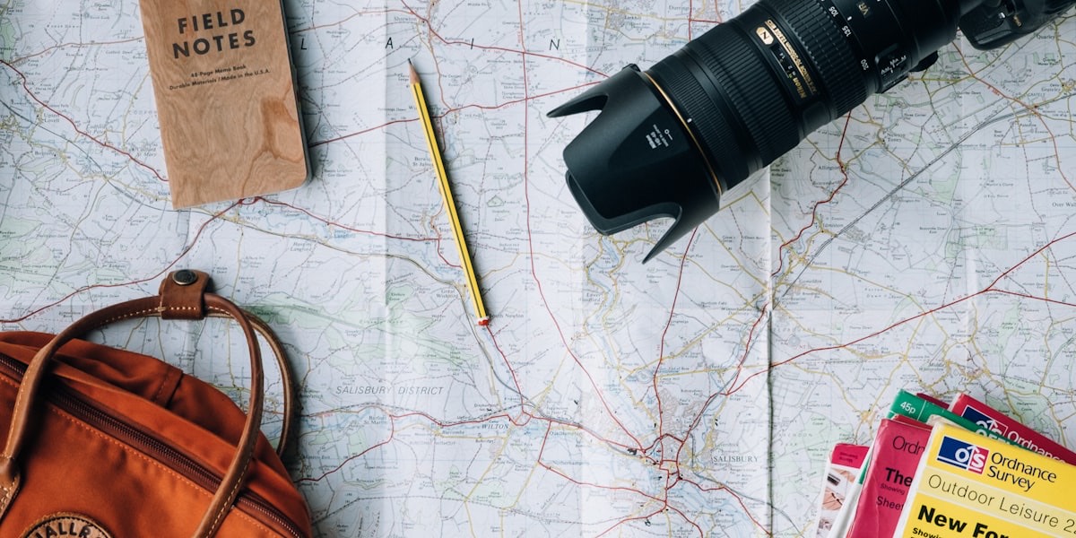 Carte routière dépliée avec un appareil photo, un carnet et un sac à dos, symbolisant la préparation d'un projet de voyage