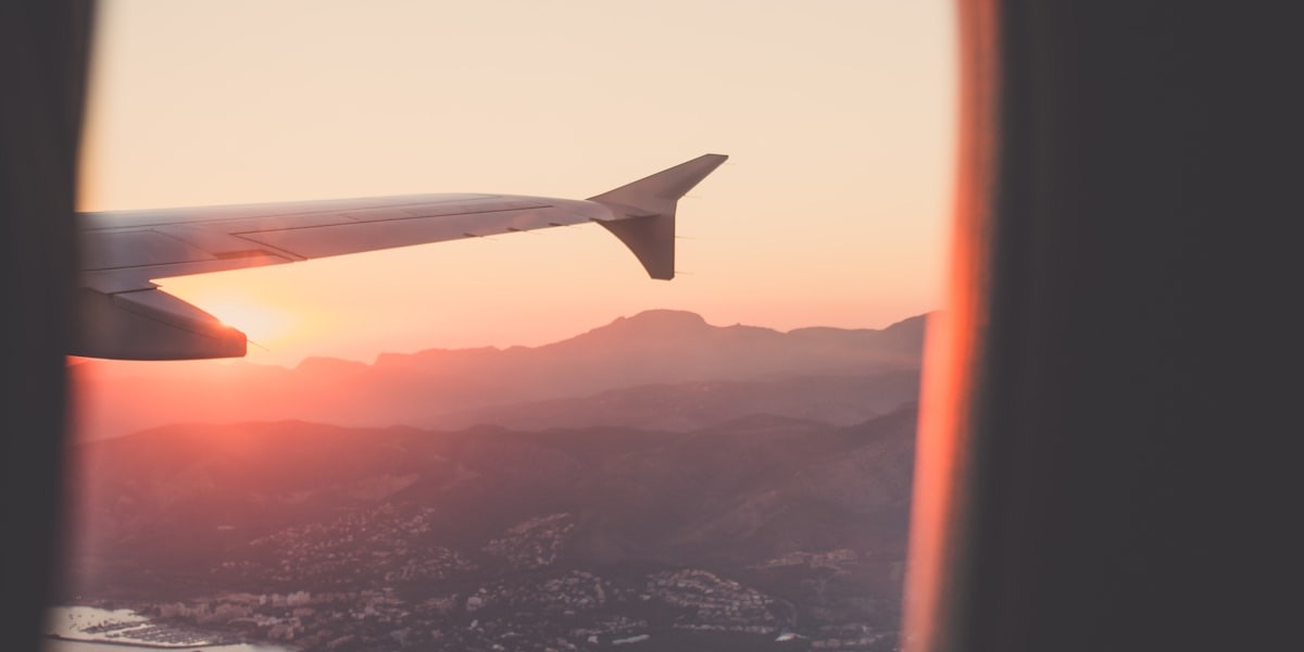 Aile d'avion vue depuis un hublot au coucher du soleil, survolant un relief montagneux